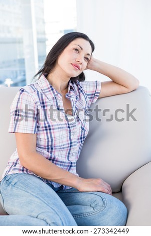 Pretty brunette thinking on couch at home in the living-room
