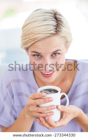Pretty blonde woman relaxing on the couch and holding a mug in the living room