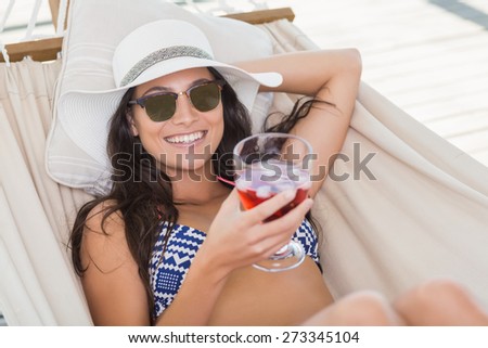 Pretty brunette relaxing on a hammock and drinking cocktail in patio