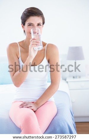 Happy brunette drinking glass of water at home in the beddroom