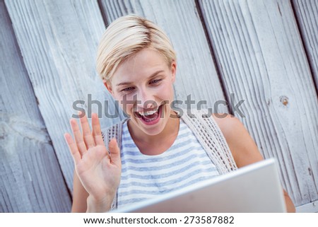 Pretty blonde woman speaking with someone online on wooden background