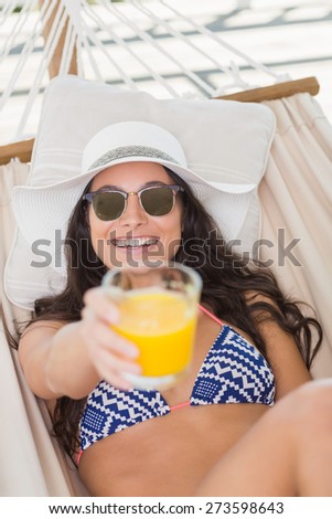 Pretty brunette relaxing on a hammock and drinking orange juice in patio