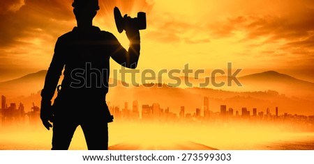 Handyman wearing tool belt while holding power drill against sun shining over road and city