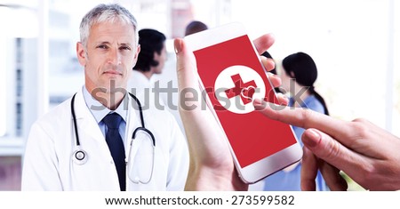Hand holding smartphone against mature doctor pointing at something on his clipboard