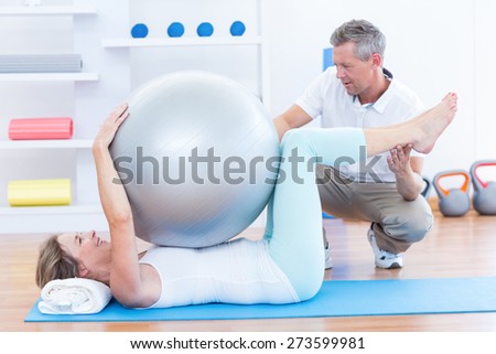 Therapist helping his patient with exercise ball in medical office