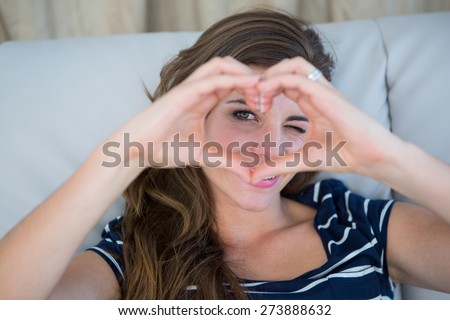 Smiling brunette making heart with her hands in the sofa