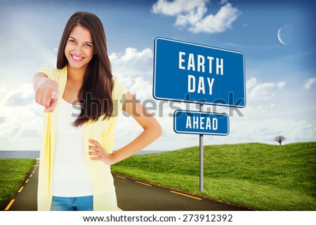Happy casual woman pointing to camera against road leading out to the horizon