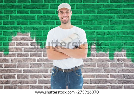 Happy man with paint roller standing arms crossed against red brick wall