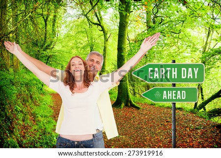 Casual couple smiling with arms raised against peaceful autumn scene in forest