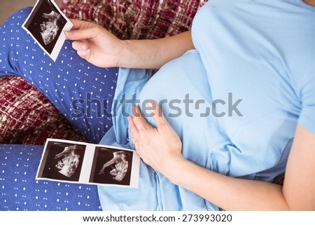 Pregnant woman looking at ultrasound scans at home in the living room