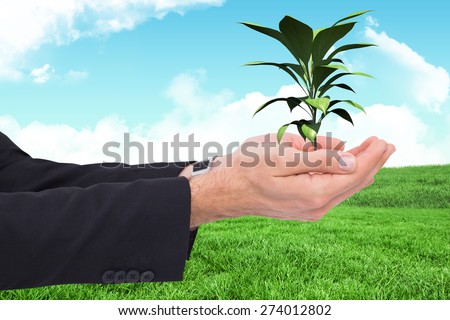 Businessman with arms out presenting something against green field under blue sky