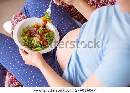 Pregnant woman eating a salad at home in the living room