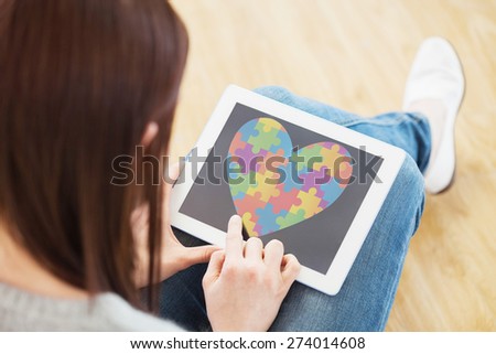 Girl using a tablet pc sitting on the floor against autism awareness heart