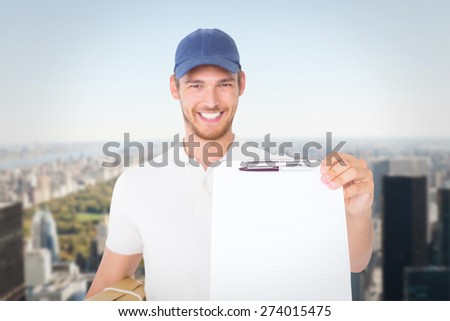 Happy delivery man holding cardboard box and clipboard against new york
