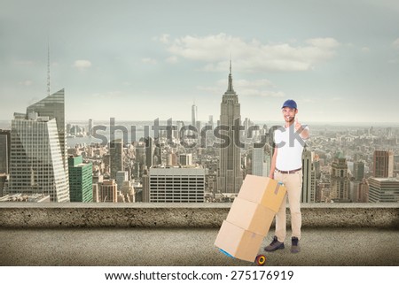 Happy delivery man pushing trolley of boxes against cityscape