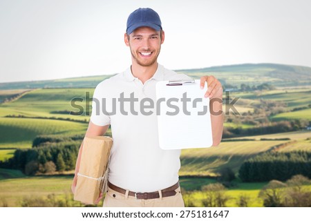 Happy delivery man holding cardboard box and clipboard against scenic landscape