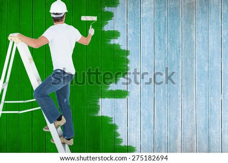Man on ladder painting with roller against wooden planks