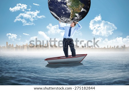 Businessman carrying the world against small boat in the sea with city on horizon