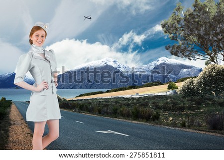 Pretty air hostess with hand on hip against scenic backdrop