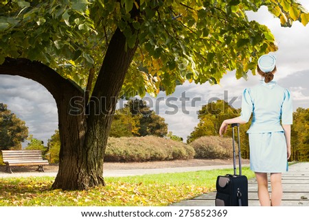 Pretty air hostess leaning on suitcase against scenic backdrop