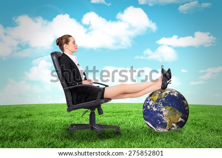 Businesswoman sitting on swivel chair with feet up against field and sky