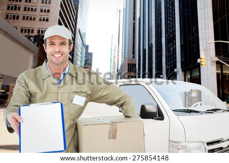 Happy delivery man with box showing clipboard against new york street