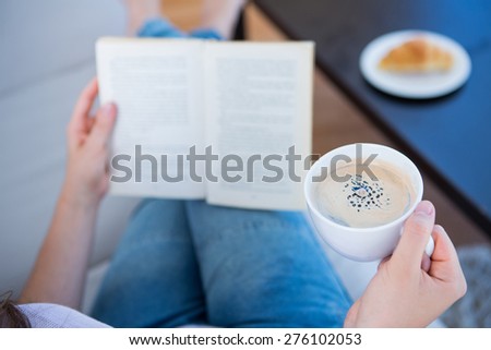 Woman reading book with cup of coffee at home in the living room