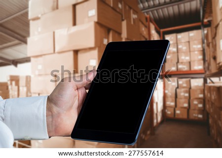 Man using tablet pc against shelves with boxes in warehouse