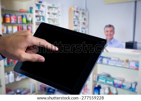 Man using tablet pc against pharmacist with grey hair standing behind shelves of drugs