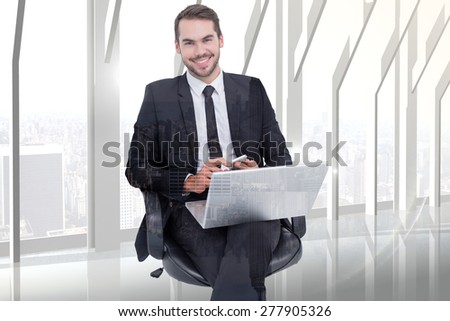 Happy businessman with laptop using smartphone against room with large window looking on city