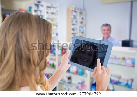 Woman using tablet pc against pharmacist with grey hair standing behind shelves of drugs