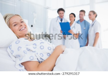 Smiling patient looking at camera with doctors behind in hospital room