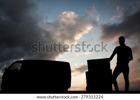 Delivery man with cardboard boxes against blue and orange sky with clouds