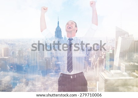 Handsome businessman cheering with arms up against city skyline