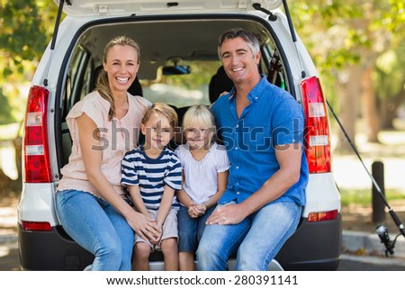 Portrait of a happy family of four sitting in car trunk while on picnic