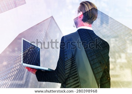 Businessman looking up holding laptop against skyscraper