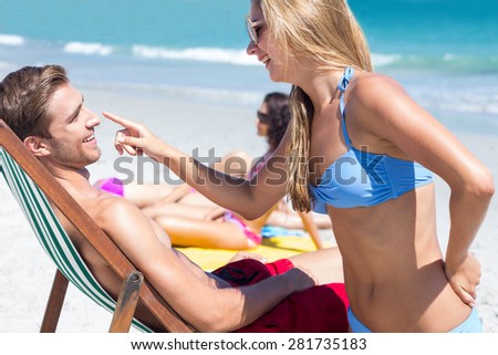 Pretty blonde putting sun tan lotion on her boyfriend at the beach