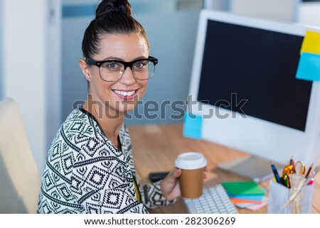 Beautiful brunette smiling at camera and holding coffee in the office