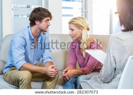 Unsmiling couple talking with their therapist in the office