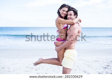 Happy couple hugging and looking at camera at the beach