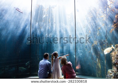 Daughter pointing a fish while her mother and father looking at fish tank at the aquarium