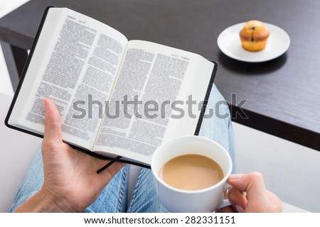 Woman reading a book and holding cup of coffee on the couch