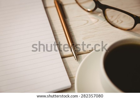 Empty notepad with reading glasses and cup of coffee on a desk