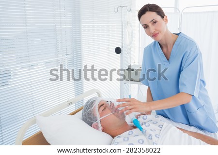 Smiling doctor holding patients oxygen mask in hospital room