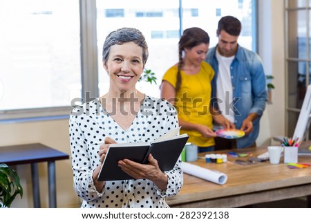 Casual businesswoman writing in diary while colleagues working in the office