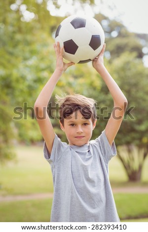 Boy looking at camera and holding a soccer ball in the park on a sunny day