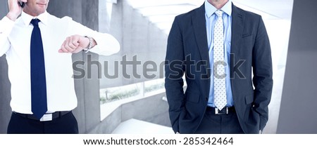 Businessman on the phone looking at his wrist watch against stylish modern home interior with staircase