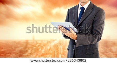 Serious charismatic businessman holding a tablet computer against sun shining over city