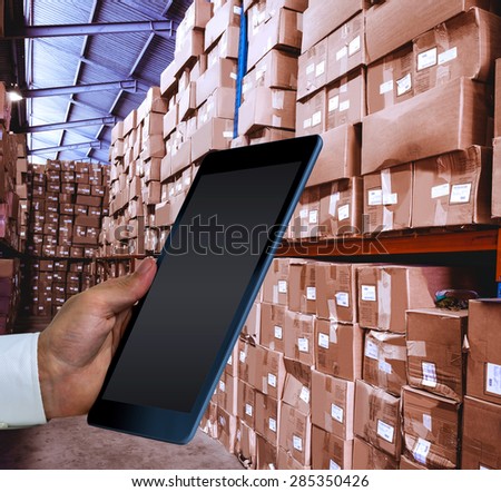 Man using tablet pc against shelves with boxes in warehouse