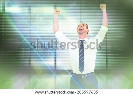 Handsome businessman cheering with arms up against window overlooking city